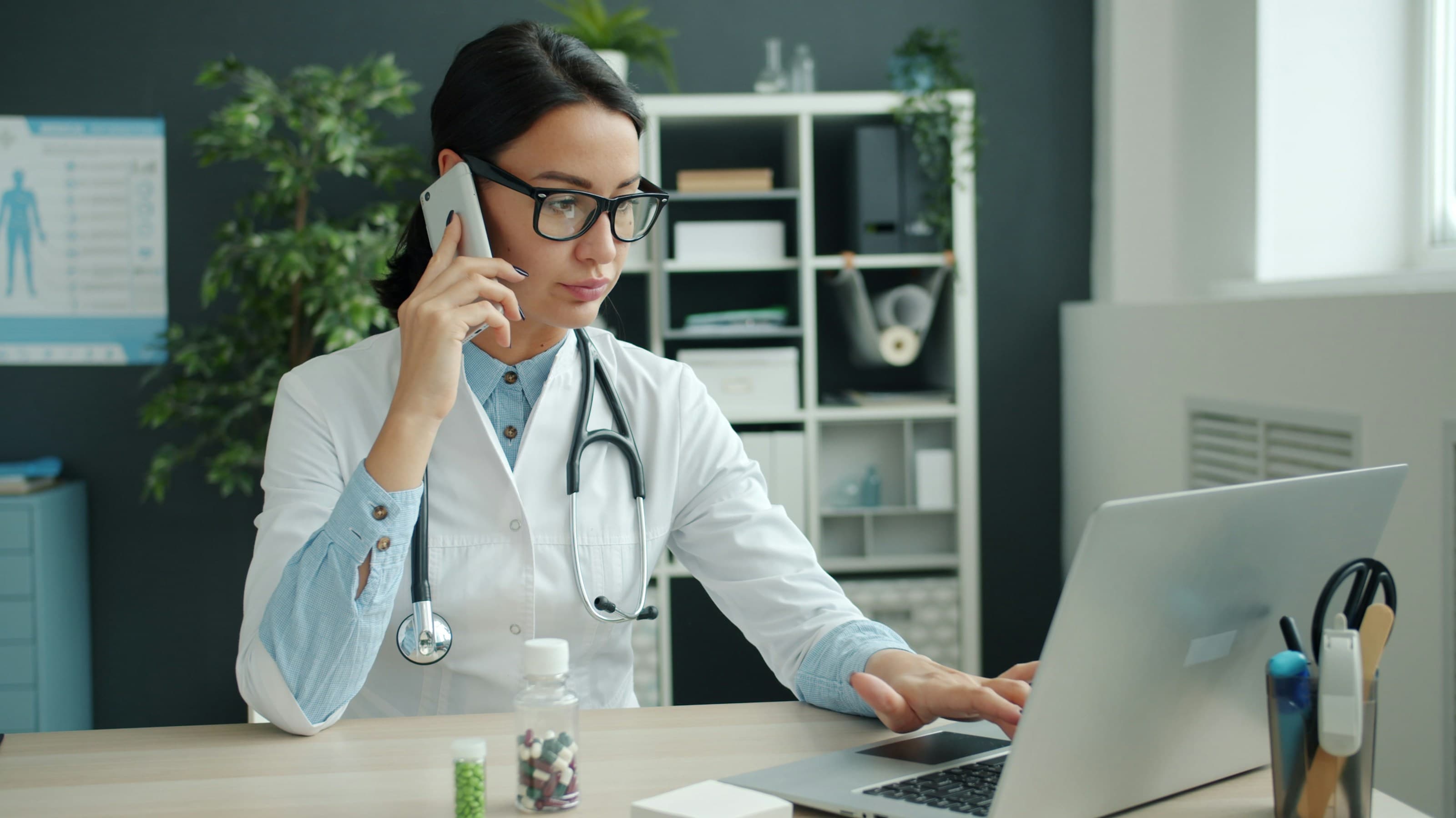 A clinician at a desk with a laptop in warm evening lamp light.
