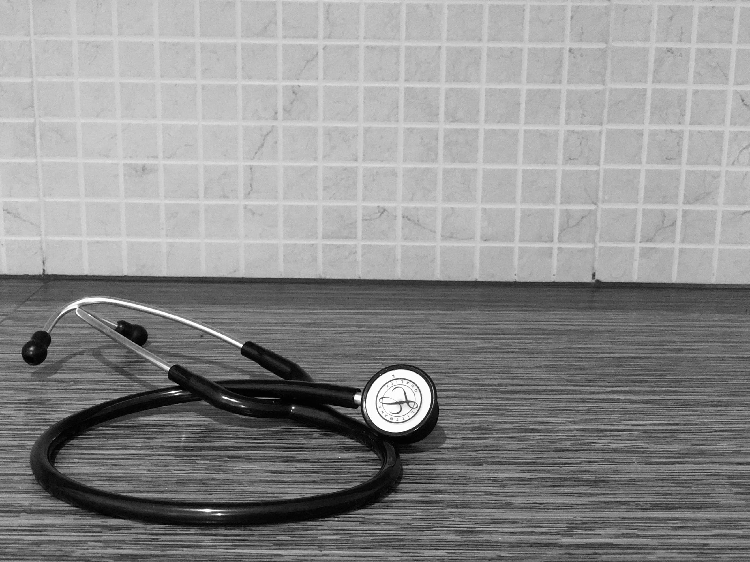 A doctor's stethoscope on a wooden desk in warm lamp light.